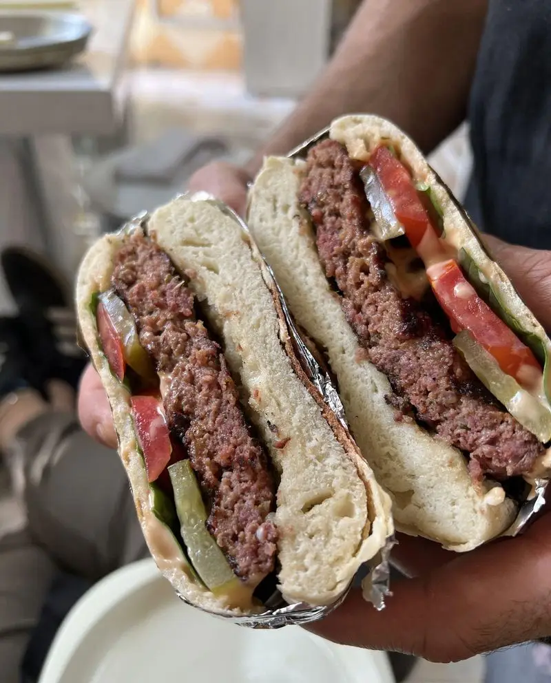 ساندویچ برگر نصف‌شده پی پزا، با پتی گوشت آبدار، گوجه، خیارشور و سس مخصوص، تجربه‌ای لذیذ در فست‌فود.