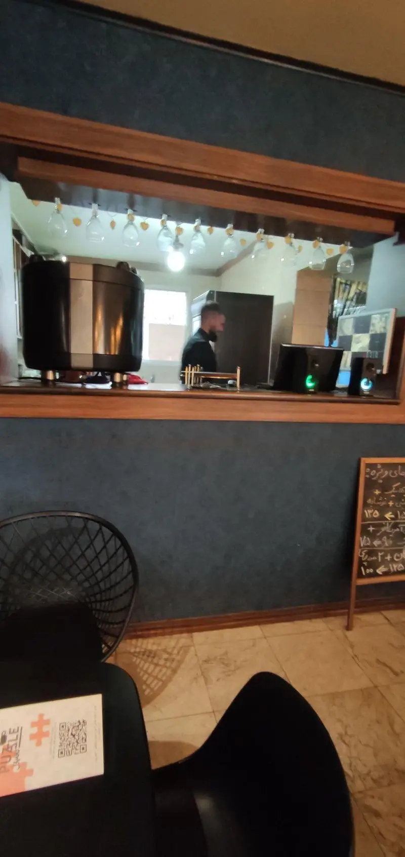 کافه پازل: فضای دنج و مدرن با باریستا حرفه‌ای پشت بار، دستگاه اسپرسو، منوی جذاب و دکوراسیون خاص لیوان‌های آویز.