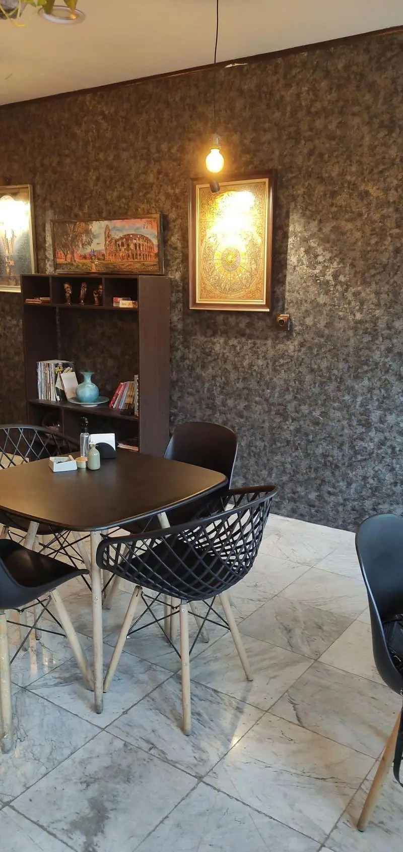 محیط دنج و زیبای کافه پازل: میز و صندلی‌های مدرن، قفسه کتاب، تابلوهای دیواری، کفپوش مرمر و نورپردازی دلنشین برای مشتریان.