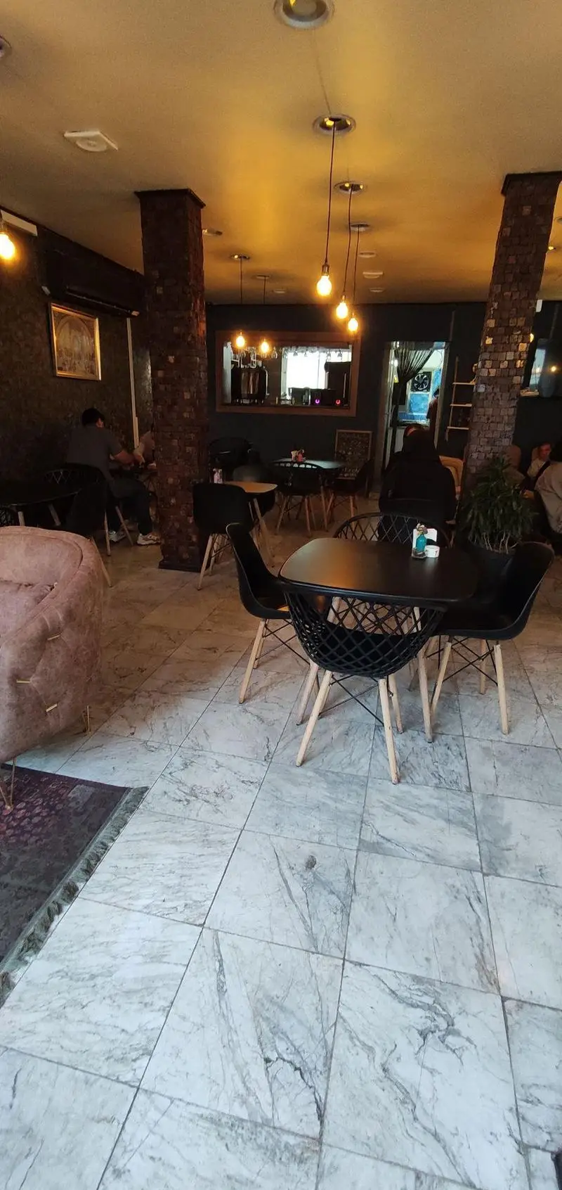 نمای داخلی دنج کافه پازل با نورپردازی گرم، میز و صندلی‌های شیک، فضایی ایده‌آل برای دورهمی و لذت بردن از نوشیدنی‌های دلخواه.