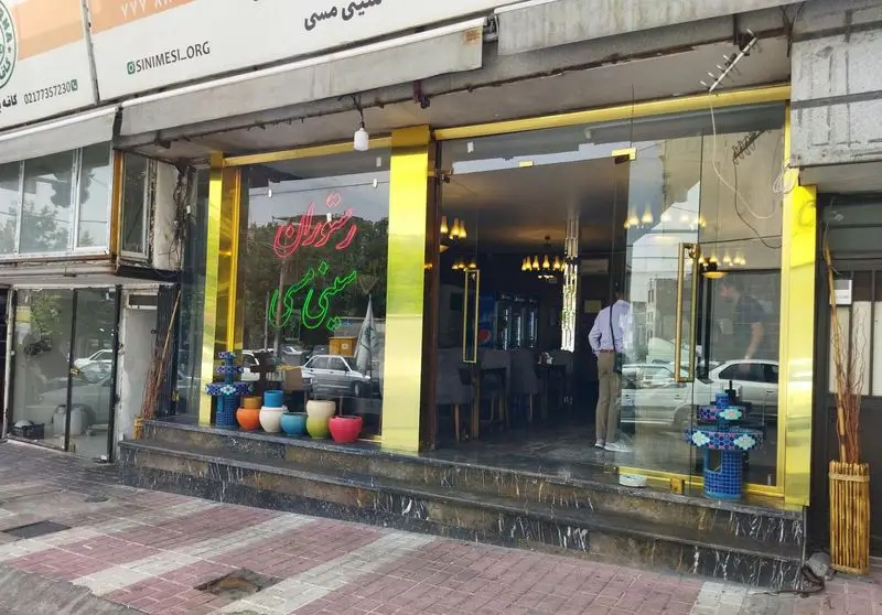 تصویر نمای بیرونی و ورودی کافه برنا، رستوران مدرن سینی مسی با طراحی شیک، فریم‌های طلایی و تابلوی نئون جذاب در تهران.