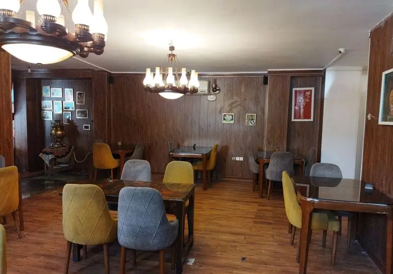 فضای داخلی کافه برنا با دیوارپوش چوبی، میز و صندلی‌های رنگی، لوسترهای سنتی و سماور برای محیطی گرم و دنج.