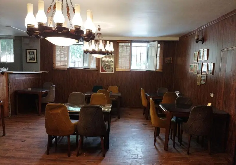 فضای داخلی کافه برنا با دکوراسیون سنتی و چوبی، لوسترهای کلاسیک، میز و صندلی‌های راحت و پنجره‌های نورگیر، محیطی گرم و دلنشین برای مشتریان.