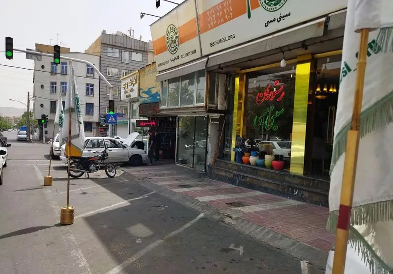 کسب و کار کافه برنا و سینی مسی در خیابان، با نمای مغازه، ویترین و تابلوی نئون. حضور خودرو، موتورسیکلت و عابرین.
