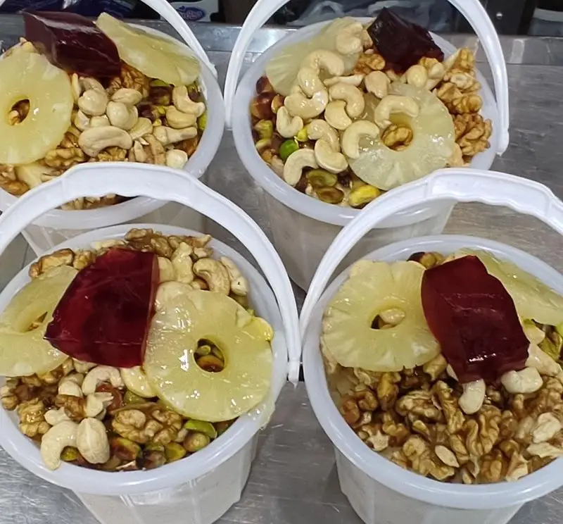 تاپینگ بستنی امید: چهار سطل پر از آجیل مخلوط (گردو، بادام هندی، پسته)، آناناس خشک و ژله قرمز میوه‌ای.