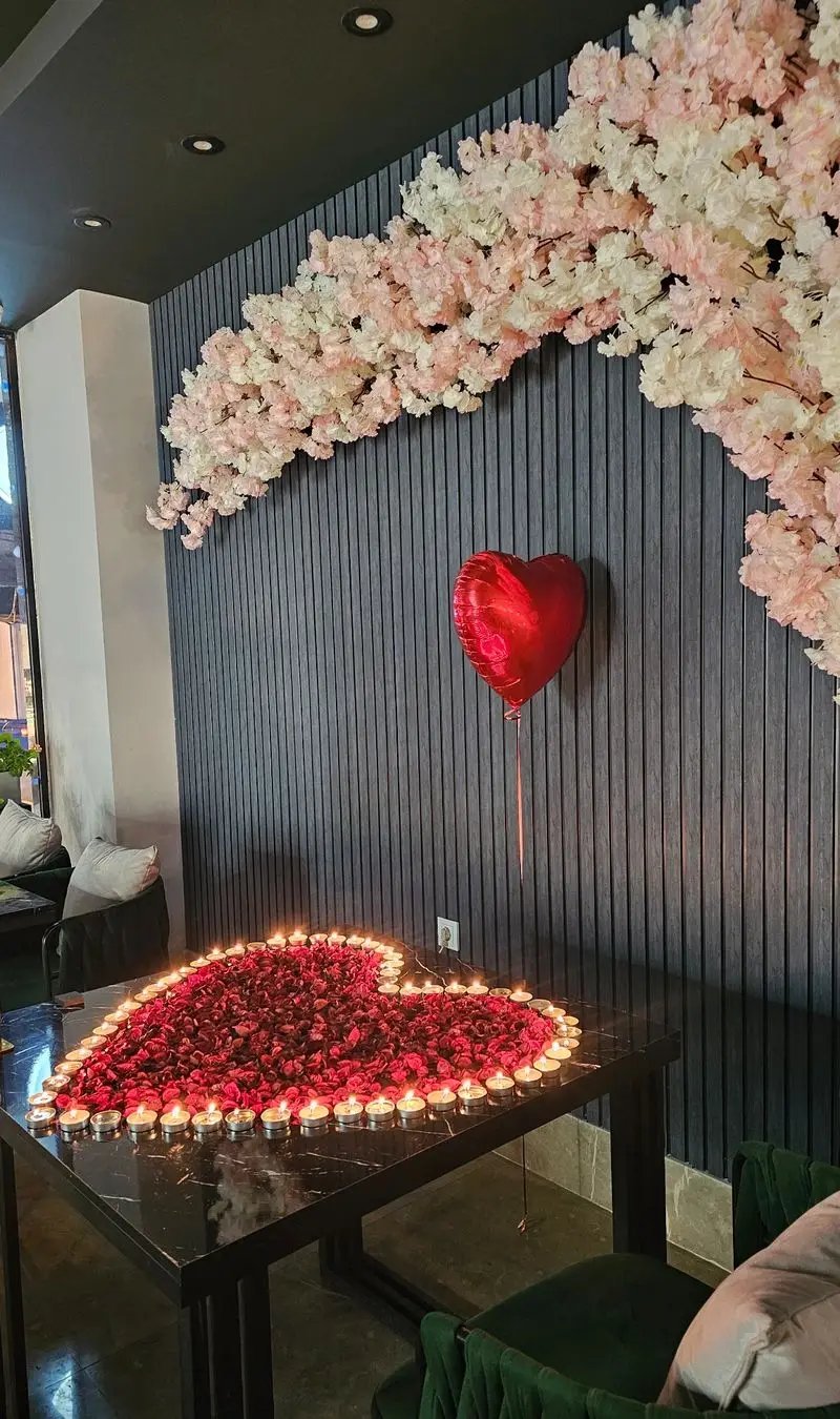 رستوران آویژه با دکوراسیون رمانتیک و دلنشین شامل گلبرگ‌های رز قرمز، شمع‌ها و بالن قلبی برای شام عاشقانه.