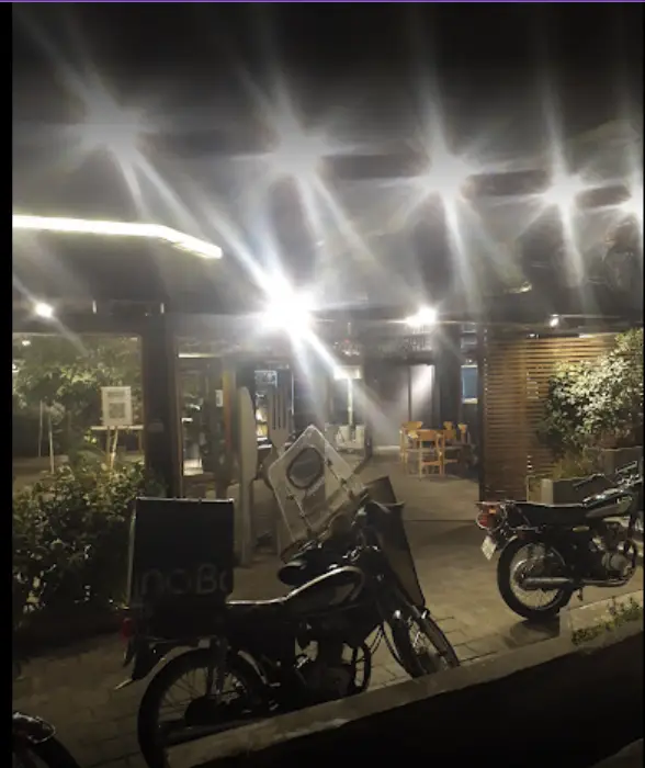 سرزمین سوخاری در شب: رستورانی با فضای باز، موتورسیکلت‌های دلیوری فعال آماده ارسال سریع سفارشات فست فود خوشمزه.