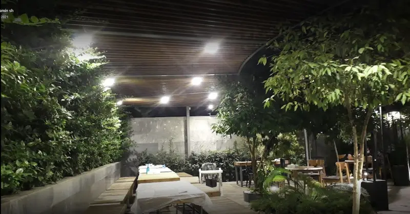 نمایی از فضای باز شبانه و سرسبز سرزمین سوخاری، با نورپردازی گرم، میز و صندلی‌های چوبی، ایده‌آل برای یک وعده غذایی دلپذیر.