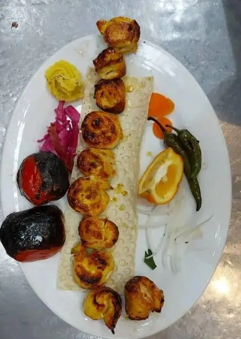 جوجه کباب لذیذ و طلایی کبابی صادق گلپایگانی سرو شده روی نان لواش با گوجه، فلفل کبابی و دورچین تازه.