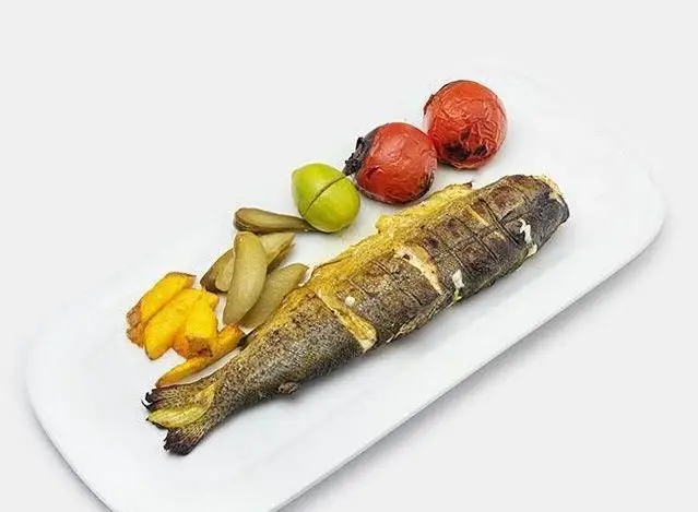 ماهی کبابی کامل و لذیذ، غذای محبوب در کبابی صادق گلپایگانی، سرو شده با سیب زمینی سرخ کرده، خیارشور، لیموترش و گوجه کبابی تازه.