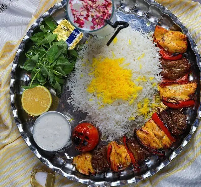 چلوکباب مخلوط جوجه و گوشت با برنج زعفرانی، گوجه، سبزی تازه، لیمو و دوغ در کافه رستوران بام ری، یک غذای اصیل ایرانی.