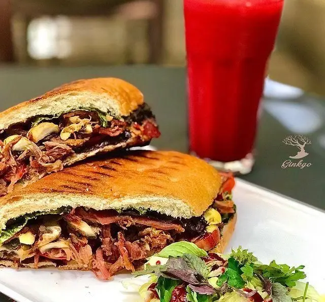 ساندویچ پانینی پرملات رستوران درخت ژینکو با گوشت پخته، قارچ و بیکن، به همراه سالاد تازه و نوشیدنی قرمز خنک.