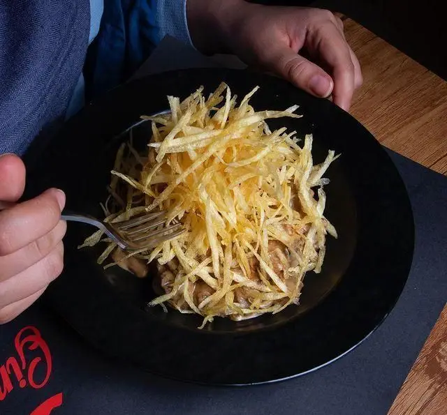 مشتری در حال لذت بردن از خوراک ویژه رستوران درخت ژینکو، با سسی خامه‌ای و سیب‌زمینی‌های خلالی ترد روی بشقاب مشکی.