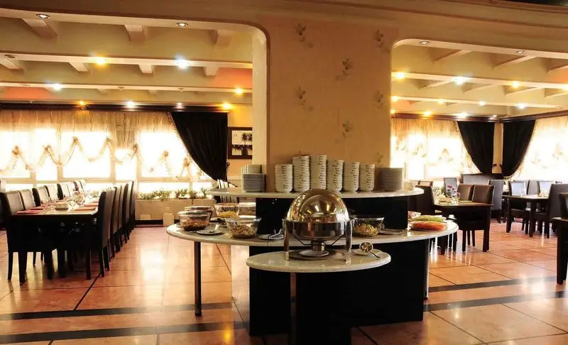 فضای داخلی شیک رستوران ارکیده طلایی با بوفه سرو غذا، میزهای غذاخوری آماده و دکوراسیون مجلل برای میزبانی مهمانان.