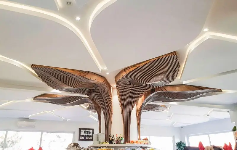 دکوراسیون داخلی لوکس و مدرن رستوران ارکیده طلایی، با سقف کاذب منحنی و نورپردازی زیبا، و سازه چوبی موج‌دار منحصر به فرد بالای بوفه غذا