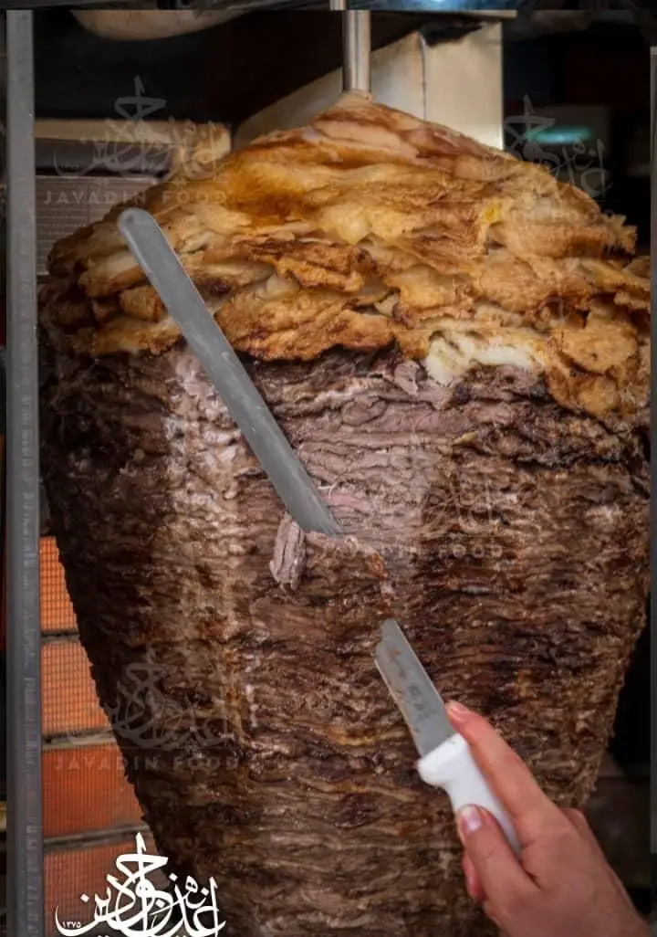 کباب ترکی ویژه جوادین: سیخ عظیم گوشت و مرغ در حال برش با چاقو برای تهیه ساندویچ‌های لذیذ.