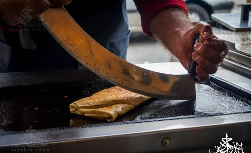 آشپز کباب ترکی جوادین در حال برش کباب دونر خوشمزه روی صفحه داغ. آماده‌سازی حرفه‌ای کباب لذیذ جوادین.