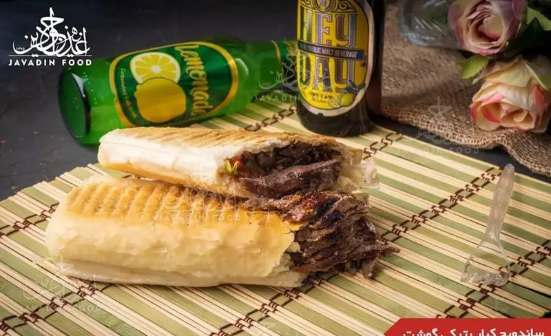 ساندویچ کباب ترکی گوشت جوادین، نان تُست شده و پر از گوشت کباب ترکی لذیذ، همراه با نوشیدنی خنک لیموناد و ماءالشعیر در رستوران جوادین.