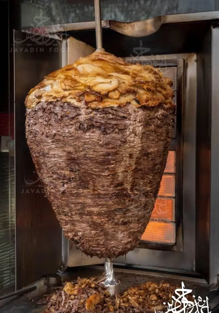 کباب ترکی دونر جوادین با لایه‌های گوشت گوساله و مرغ بریان شده در حال پخت روی سیخ عمودی، آماده برای سرو در رستوران جوادین.