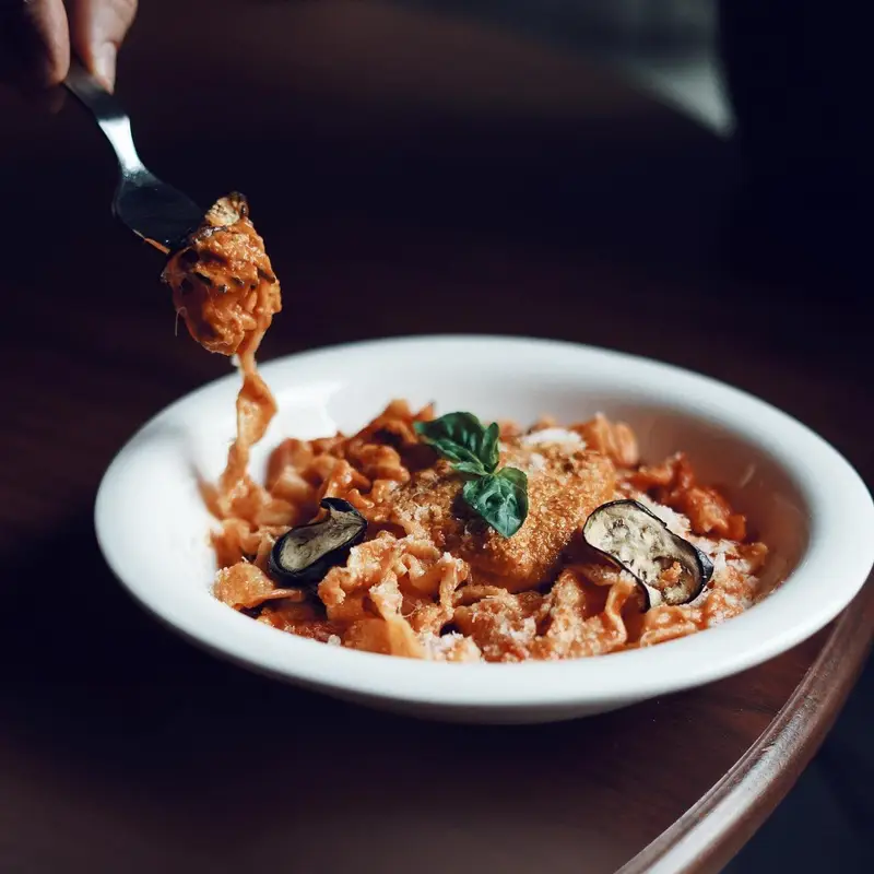 یک چنگال پاستا با سس لذیذ و بادمجان سرخ شده، برداشته شده از کاسه. تجربه‌ای دلنشین در کافه رستوران ایتالیایی ژینر