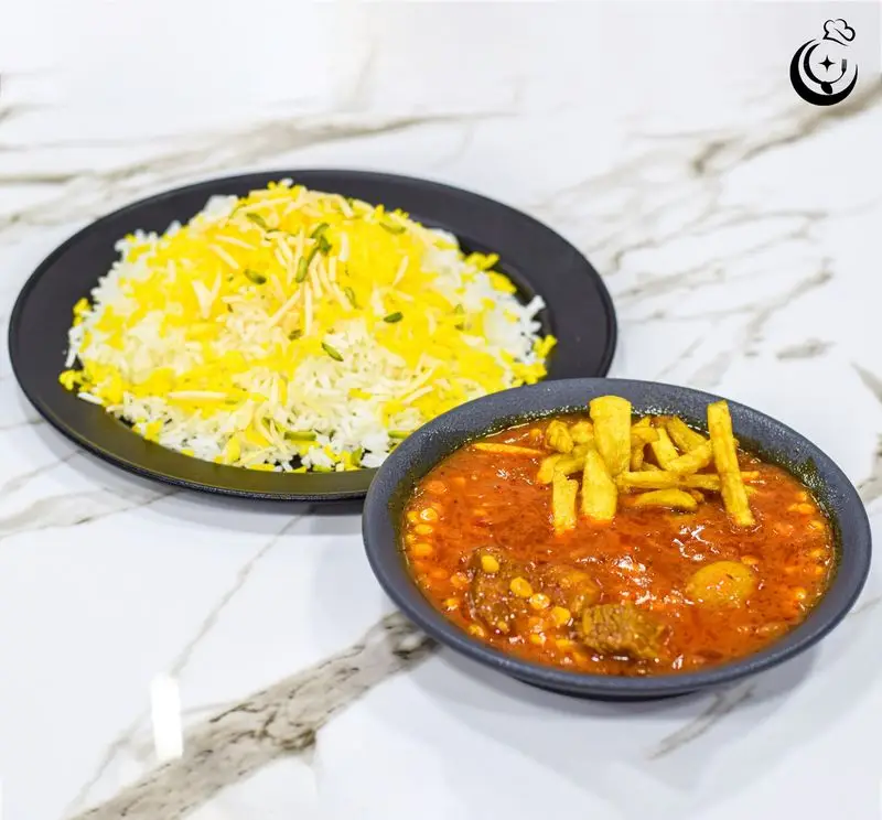 غذای سنتی و خوشمزه رستوران کترینگ آسمان شامل چلو خورش قیمه با گوشت و لپه، تزئین شده با سیب‌زمینی سرخ کرده و برنج زعفرانی با خلال پسته روی میز مرمر سفید.