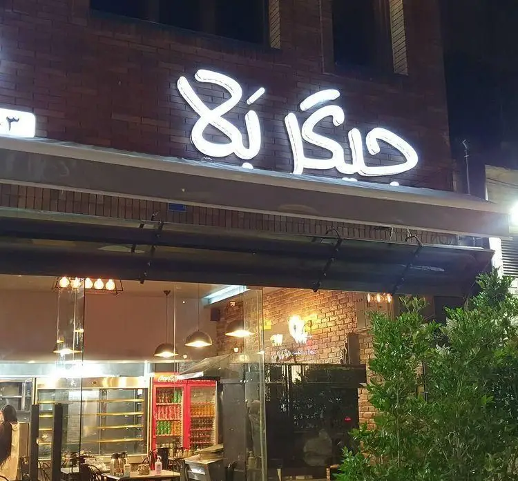 تصویری از نمای شبانه رستوران جیگر بلا با تابلوی نئونی روشن و دیوارهای آجری. داخل رستوران با نورپردازی گرم مشخص است.