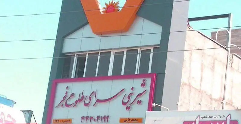 شیرینی سرای طلوع فجر، نمای بیرونی قنادی معروف با تابلوی درخشان، عرضه کننده مرغوب‌ترین شیرینی‌ها، کیک و دسرهای ایرانی.