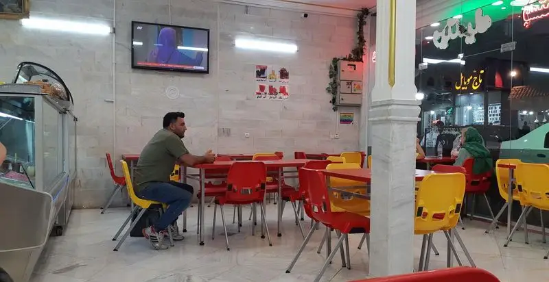 تصویر داخلی بستنی عمو، مکانی شاد و مدرن با چیدمان میز و صندلی‌های قرمز و زرد، جایی عالی برای دورهمی و چشیدن بستنی‌ها و دسرهای لذیذ و متنوع در شهر.