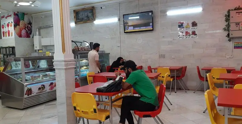 تصویری از بستنی فروشی عمو، محیطی دوستانه با دکوراسیون رنگارنگ، یخچال نمایش بستنی، و مشتریانی که از دسر لذت می‌برند.