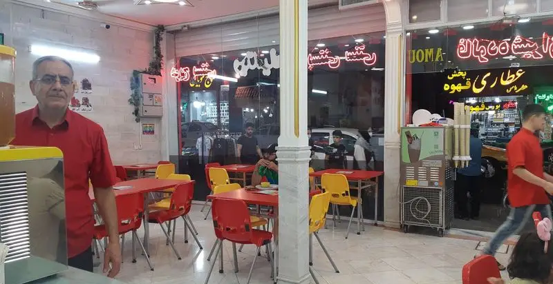 تصویری از فضای داخلی شلوغ بستنی عمو. مردی در لباس قرمز پشت پیشخوان، میز و صندلی‌های قرمز و زرد، مشتریان و ویترین مغازه مجاور دیده می‌شود.