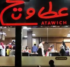 نمای بیرونی رستوران فست فود عطاویچ در شب با تابلوی روشن و مشتریانی که در حال لذت بردن از فضای داخلی و غذا هستند.