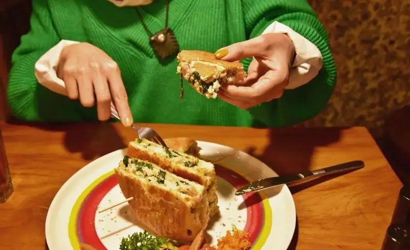 تصویری از مشتری در کافه وصال، در حال لذت بردن از یک ساندویچ خوشمزه با فیلینگ تازه، نشانگر محیطی دلنشین و غذایی با کیفیت.