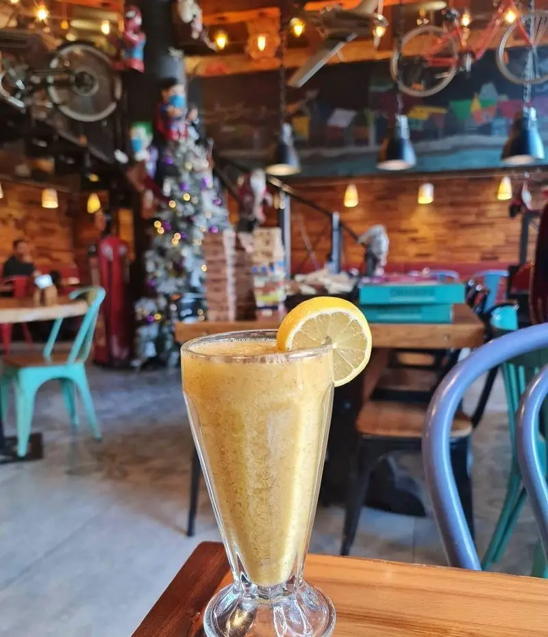 یک لیوان اسموتی تازه و دلچسب در کافه وصال، با دکوراسیون داخلی منحصر به فرد شامل درخت کریسمس، دوچرخه‌های آویزان و فضای گرم و صمیمی.