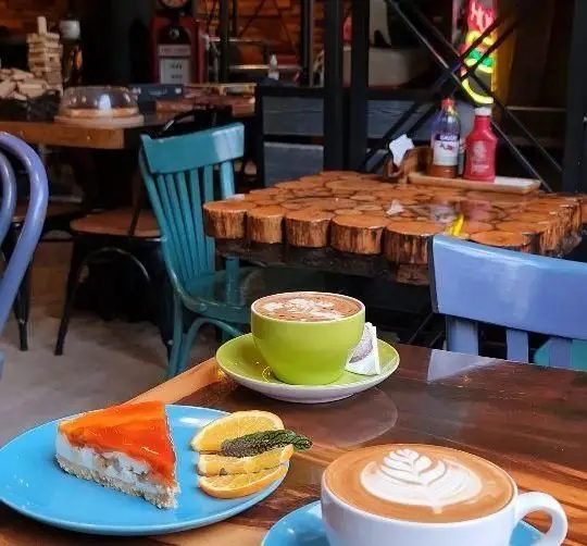 کافه وصال: فضایی دلنشین با میز چوبی منحصربه‌فرد، دو فنجان لاته آرت زیبا و یک برش کیک پنیر پرتقالی خوش‌طعم، مناسب برای دورهمی و کافه گردی.