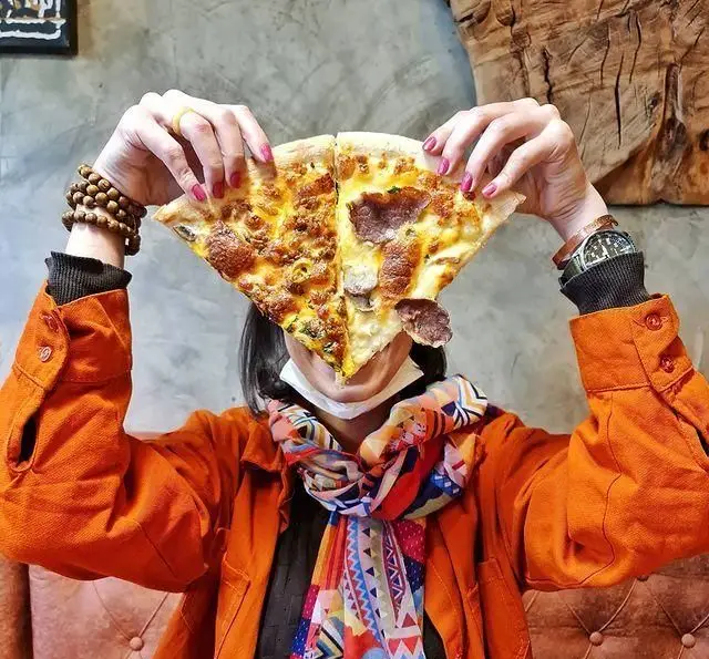 مشتری کافه وصال با دو برش پیتزای خوشمزه و متنوع که صورتش را پوشانده، تجربه ای متفاوت و شاد در این کافه.