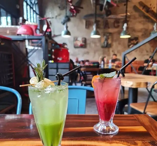 تصویری جذاب از نوشیدنی‌های خنک و میوه‌ای کافه وصال، شامل یک موهیتو سبز و شربتی قرمز در محیطی مدرن و دنج با دکوراسیون خاص.