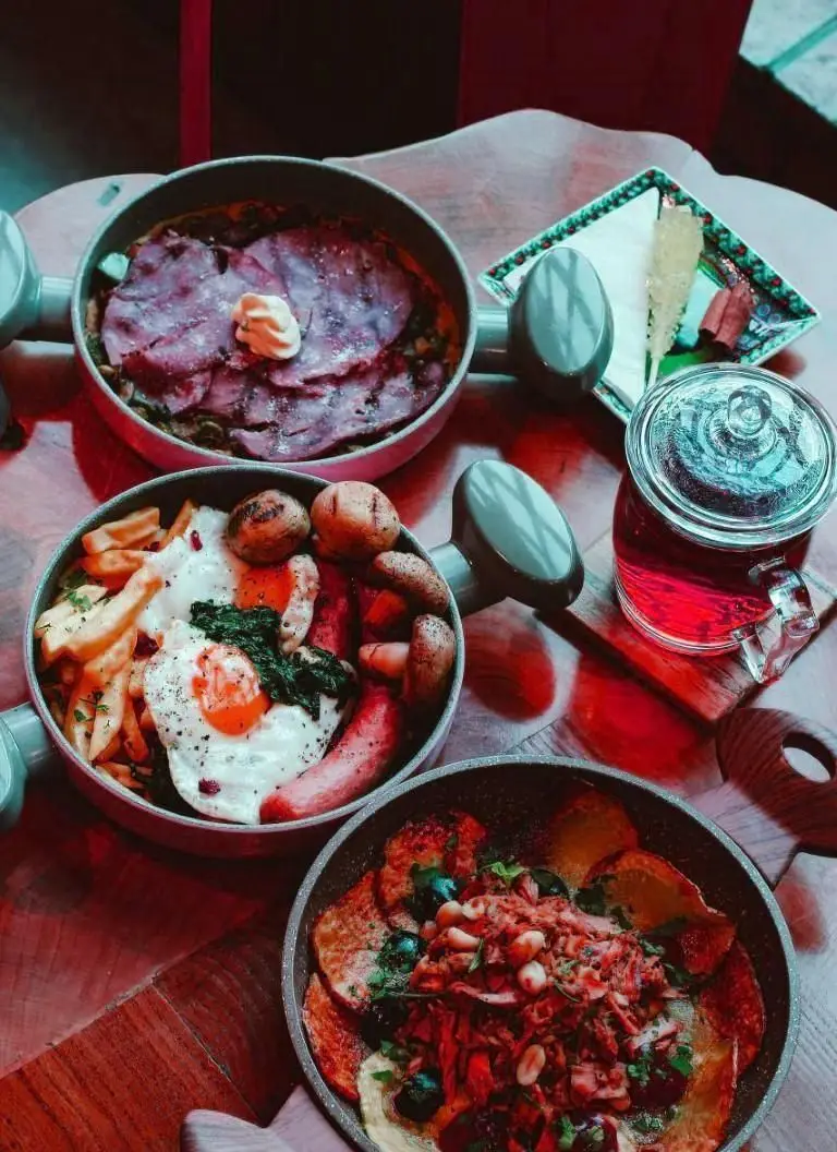 میز صبحانه لذیذ کافه وصال با خوراک‌های متنوع؛ شامل بیکن، املت، سوسیس، تخم مرغ نیمرو، سیب‌زمینی و چای داغ.