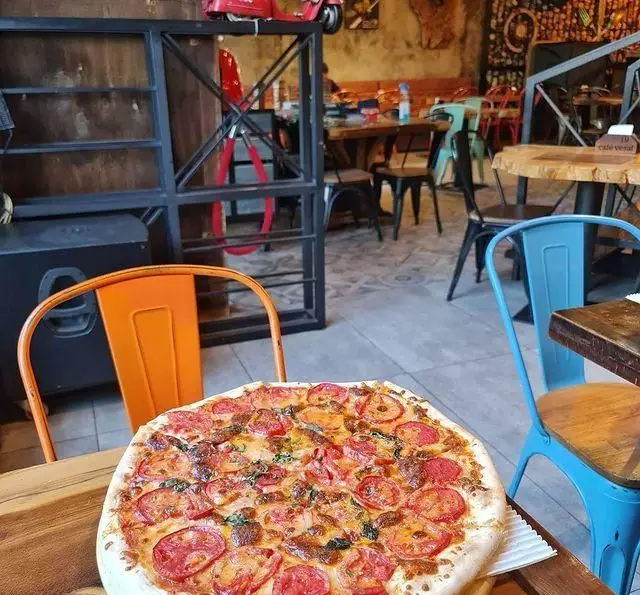 پیتزا بزرگ با گوجه، ریحان و پنیر در کافه وصال، فضایی گرم و دلنشین برای صرف یک وعده غذای تازه و خوشمزه با دوستان.