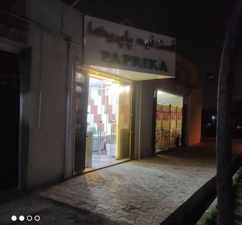 نمای بیرونی فروشگاه پاپریکا در شب با تابلوی روشن "PAPRIKA" به فارسی و انگلیسی، نشاندهنده ورودی کسب و کار.
