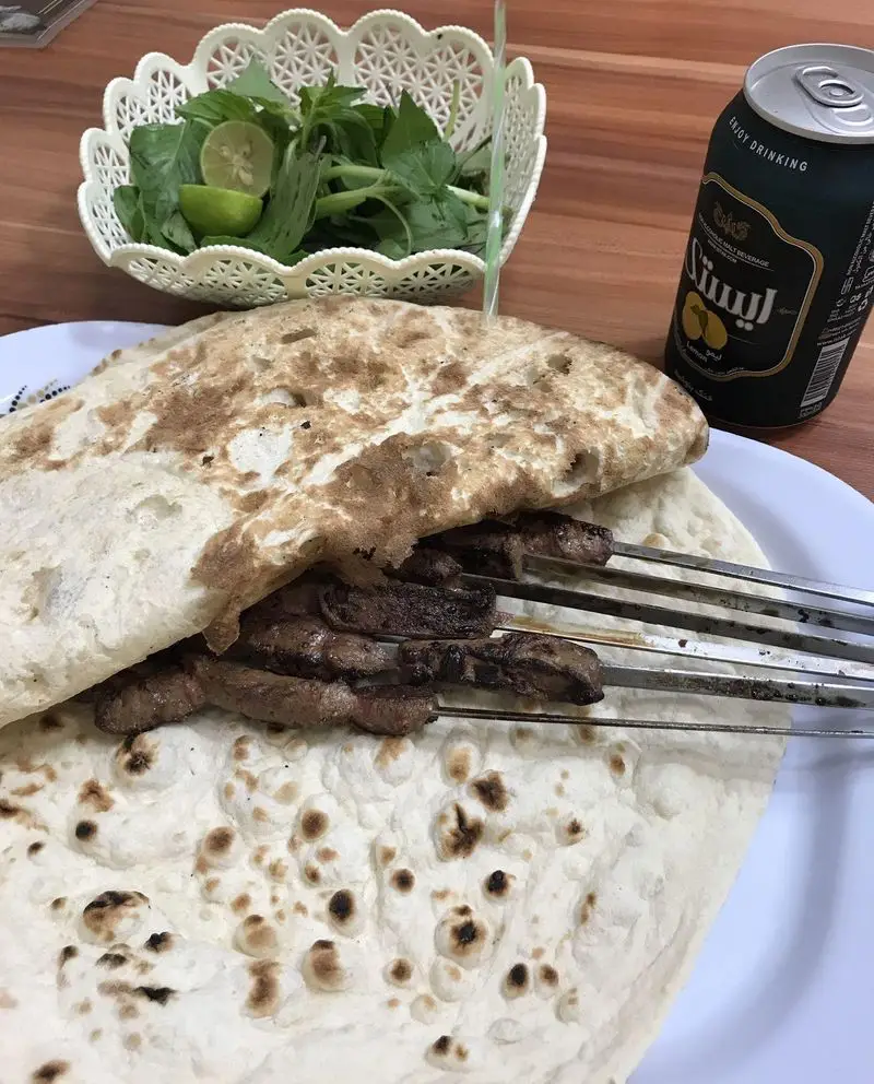 جگر کباب‌های خوشمزه جگر سرای ملاصدرا، سرو شده روی نان تازه، همراه با ظرفی از سبزی خوردن، لیمو و نوشیدنی مالت.