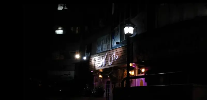 تصویر شبانه از نمای بیرونی های کافه با تابلوی روشن چوبی و نورپردازی دلنشین، فضایی گرم و دعوت‌کننده برای مشتریان.