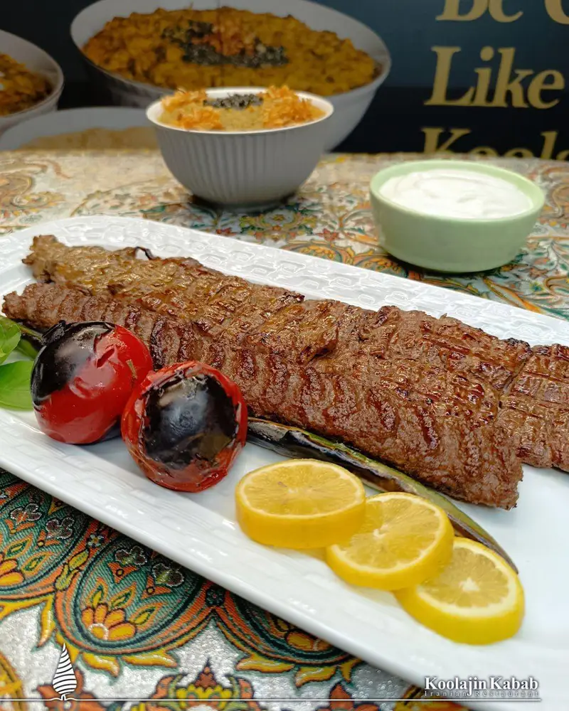 تصویری جذاب از کباب برگ و کوبیده اصیل ایرانی در بشقاب سفید، با گوجه و لیمو، در رستوران آش و حلیم کولاژین سعادت آباد.