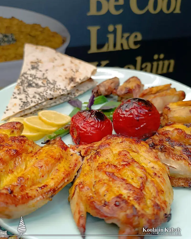 یک بشقاب جوجه کباب خوشرنگ از رستوران آش و حلیم کولاژین در سعادت آباد با گوجه کبابی، نان و لیمو. تجربه غذای ایرانی عالی.