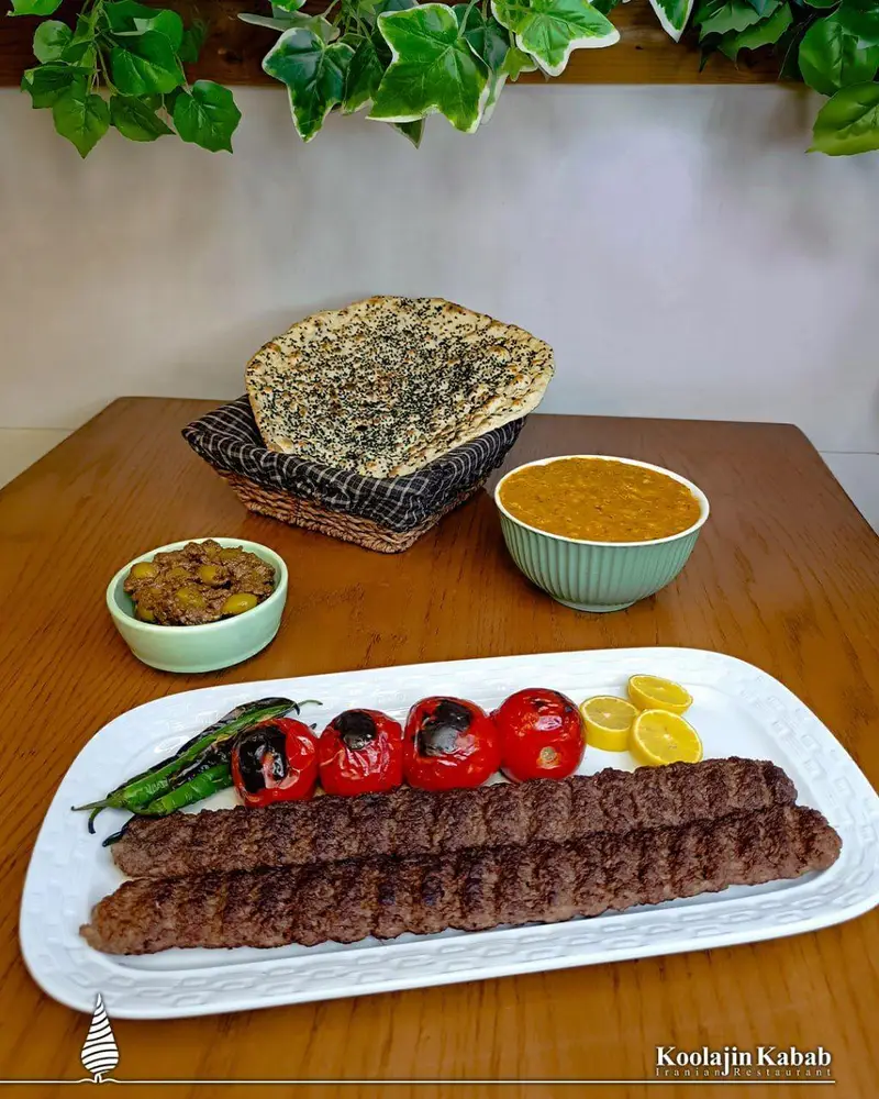 تصویری از میز غذا شامل کباب کوبیده آبدار، گوجه و فلفل کبابی، زیتون پرورده، نان تازه و آش کولاژین سعادت آباد.