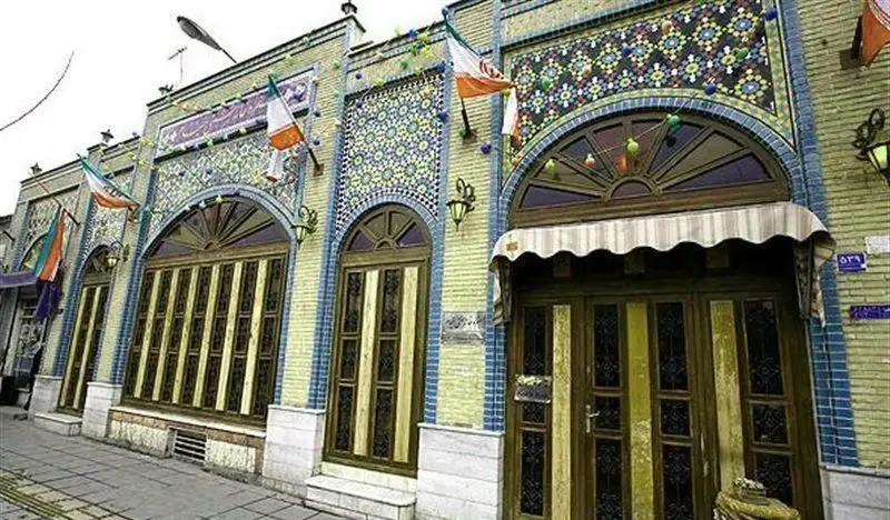 نمای بیرونی رستوران سنتی خیام با کاشی‌کاری فیروزه‌ای و معماری اصیل ایرانی. دکوراسیون سنتی و پرچم‌های ایران.