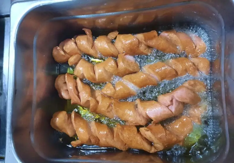 هات داگ‌های مارپیچ و خوشرنگ در حال سرخ شدن در روغن داغ، آماده سازی لذیذترین ساندویچ‌های پیتزا ساندویچ آیدا.