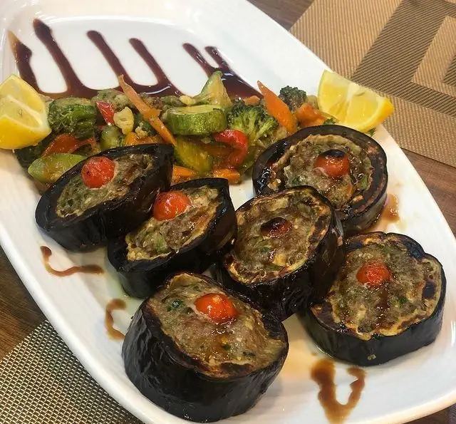 بشقاب دلمه بادمجان شکم‌پر با گوشت و سبزیجات، تزئین با گوجه گیلاسی و لیمو، همراه میکس سبزیجات تازه و سس مخصوص رستوران رزماری.