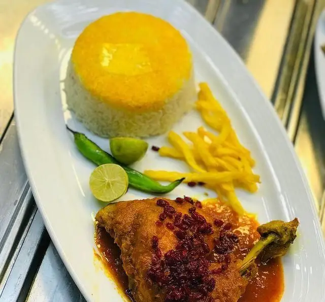 غذای لذیذ زرشک پلو با مرغ رستوران رزماری شامل برنج زعفرانی، مرغ آبدار، زرشک، سیب زمینی و فلفل سبز تازه.