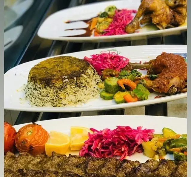 سفره‌ای پر از غذاهای اصیل ایرانی در رستوران رزماری: کباب کوبیده، ته دیگ پلو شوید با مرغ، گوجه کبابی و ترشی‌های رنگارنگ
