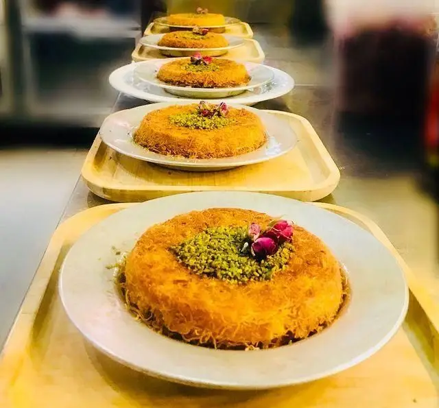 کنافه های لذیذ و دلنشین رستوران رزماری، دسری محبوب خاورمیانه ای با تزیین پسته و غنچه های رز، در سینی های چوبی زیبا.